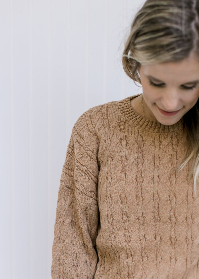 Close up of cable knit on a camel colored sweater with a round neck and long sleeves. 