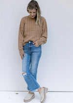 Model wearing jeans with a camel sweater with a round neck, long sleeves and a cable knit fabric. 