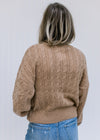Back view of Model wearing a camel sweater with a round neck, long sleeves and a cable knit fabric.
