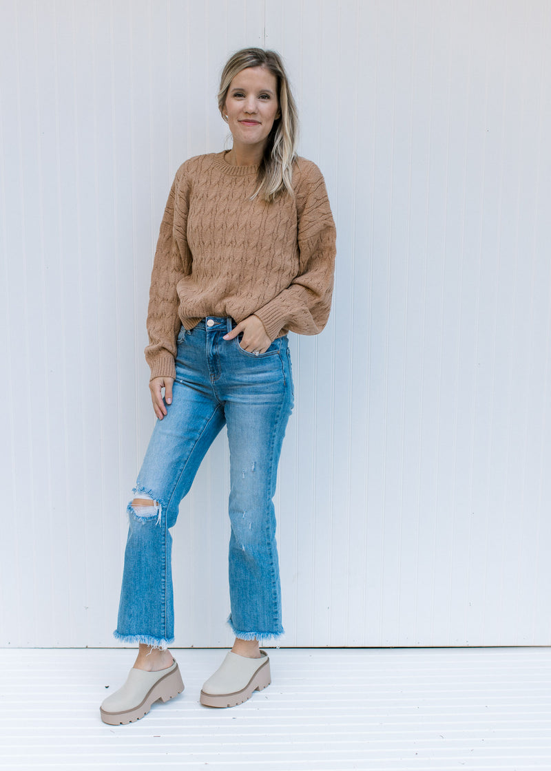 Model wearing jeans and mules with a long sleeve camel sweater with a cable knit fabric. 