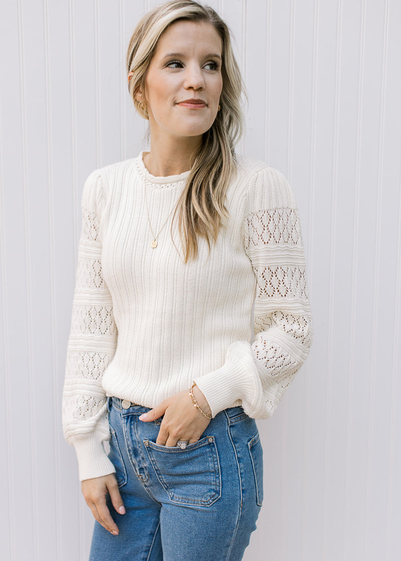 Model wearing a cream sweater with a ribbed bodice, eyelet detail on long sleeves. 