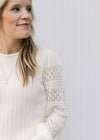 Close up of eyelet detail on long sleeve of a cream ribbed sweater with a round neck. 