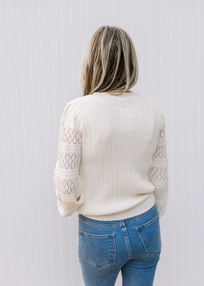 Back view of Model wearing a cream sweater with a ribbed bodice, eyelet detail on long sleeves. 