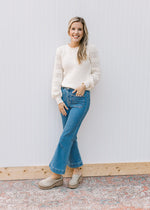 Model wearing jeans with a cream sweater with a ribbed bodice, eyelet detail on long sleeves. 