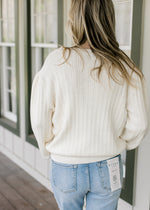 Back view of Model wearing a long sleeve cream sweater with embroidered flower motif.