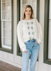 Model wearing a cream boat neck sweater with embroidered flower motif and long sleeves. 