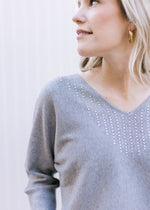 Close up of silver sequins at the neck of v-neck on a soft heather gray sweater with long sleeves.