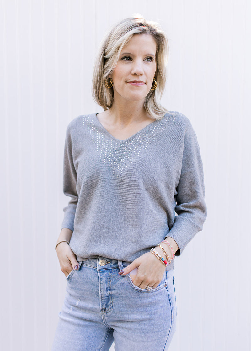 Model wearing a soft heather gray sweater with silver sequins at the v-neck and long sleeves.