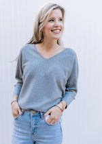 Model wearing jeans and a soft heather gray long sleeve sweater with silver sequins at the v-neck.