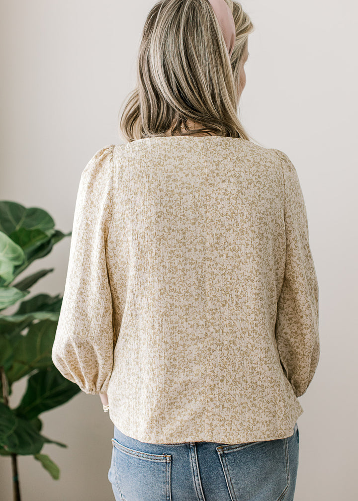 Back view of Model wearing a white top with taupe ditsy floral, boat neck, buttons and 3/4 sleeves. 