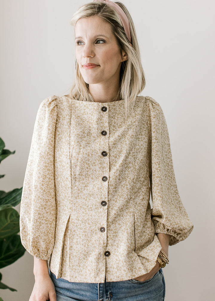 Model wearing a white top with taupe ditsy floral, boat neck, pleated hem and 3/4-bubble sleeves. 