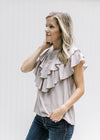 Model wearing a stone colored top with a button up back, cap sleeves and double ruffle detail. 