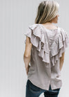 Back view of button up closure and double ruffle detail on a stone colored top with cap sleeves. 