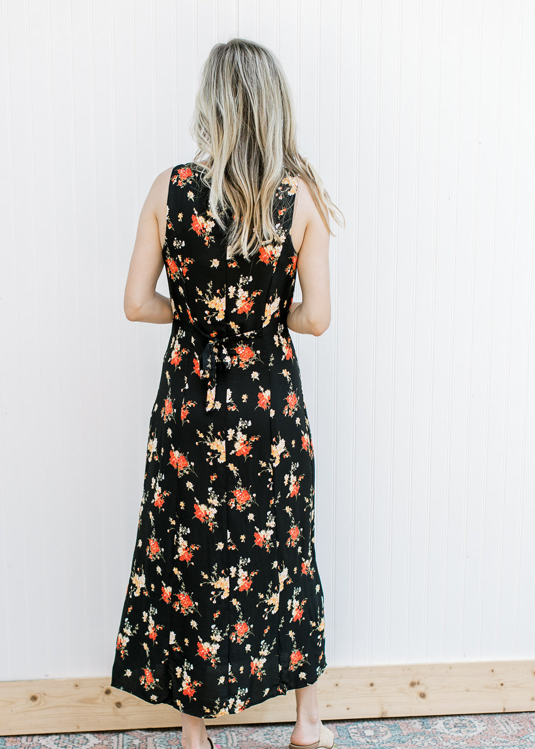 Back view of Model wearing a sleeveless black maxi with yellow and red floral a button front.