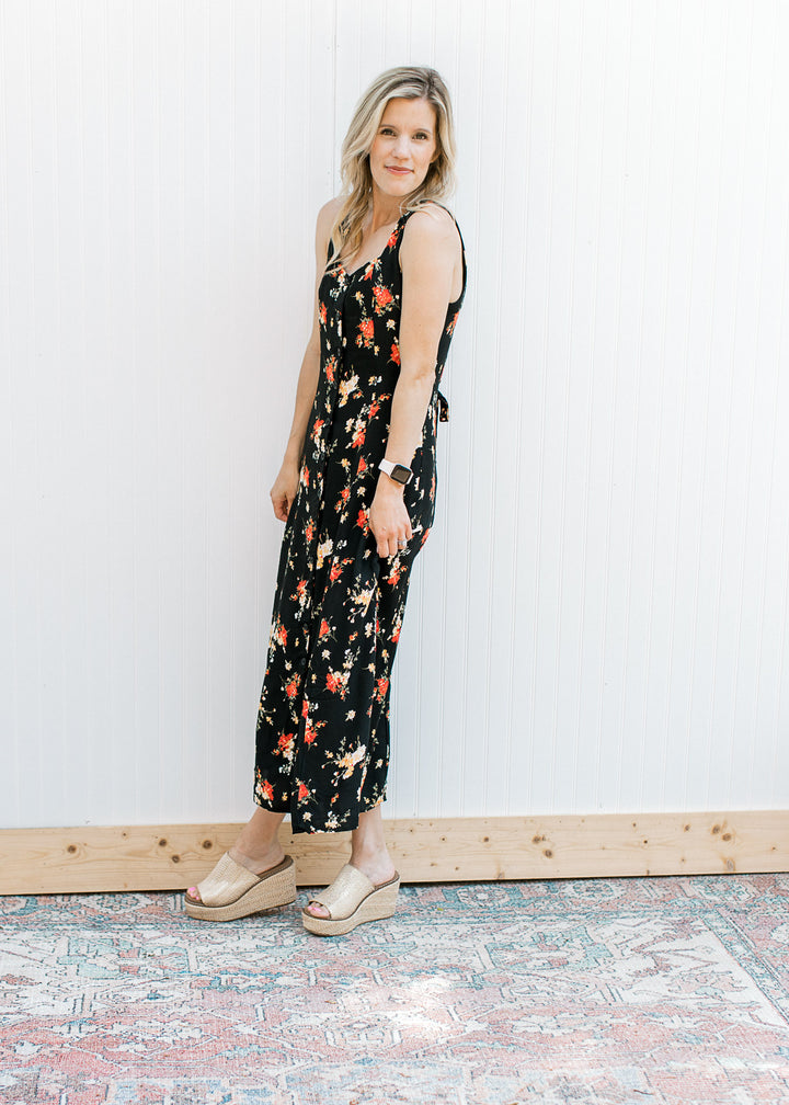 Model wearing wedges and a sleeveless black maxi with yellow and red floral a button front.