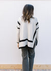 Back view of Model wearing a cream sweater with black outline, mocked neck and long sleeves. 