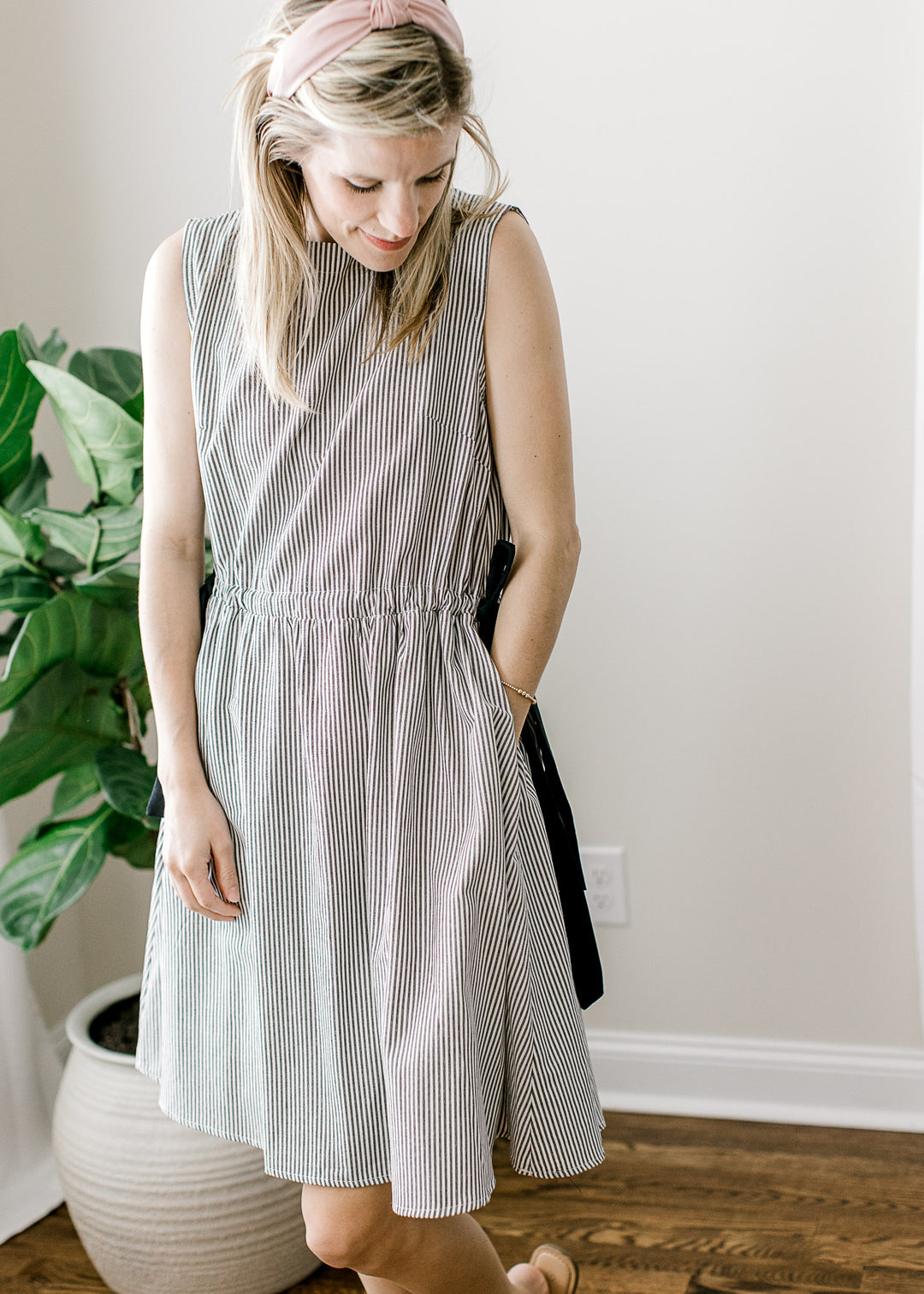 Model wearing a sleeveless black and white striped dress with a boat neck and pockets. 