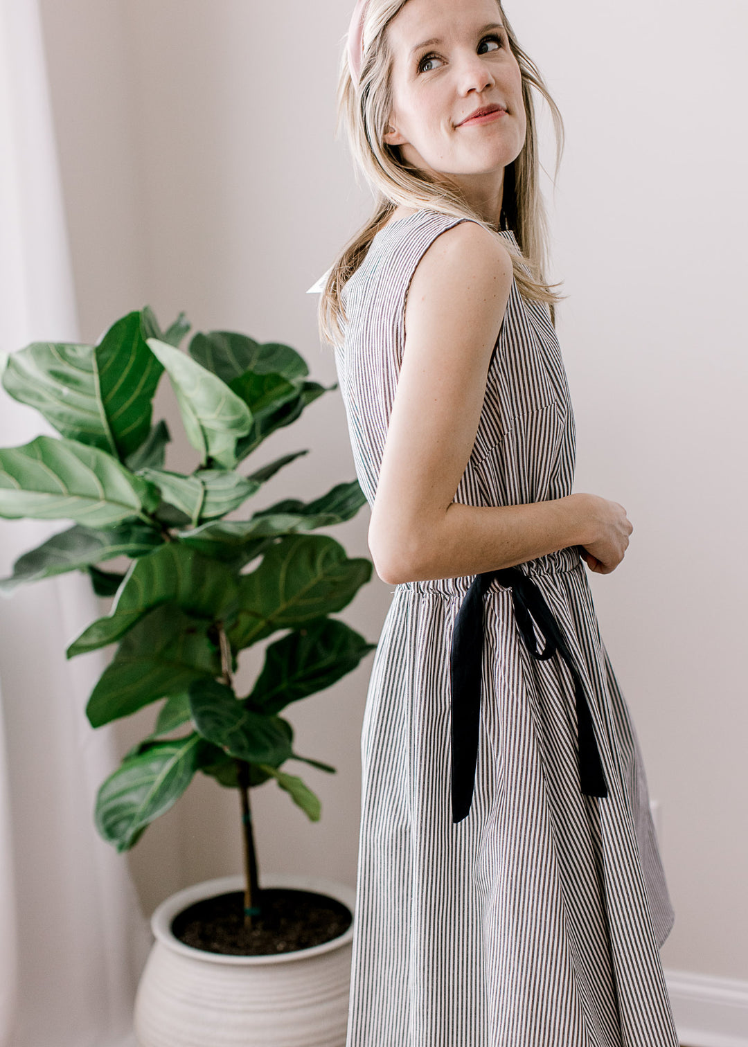 Side view of model wearing a black and white striped dress with adjustable side ties at waist.