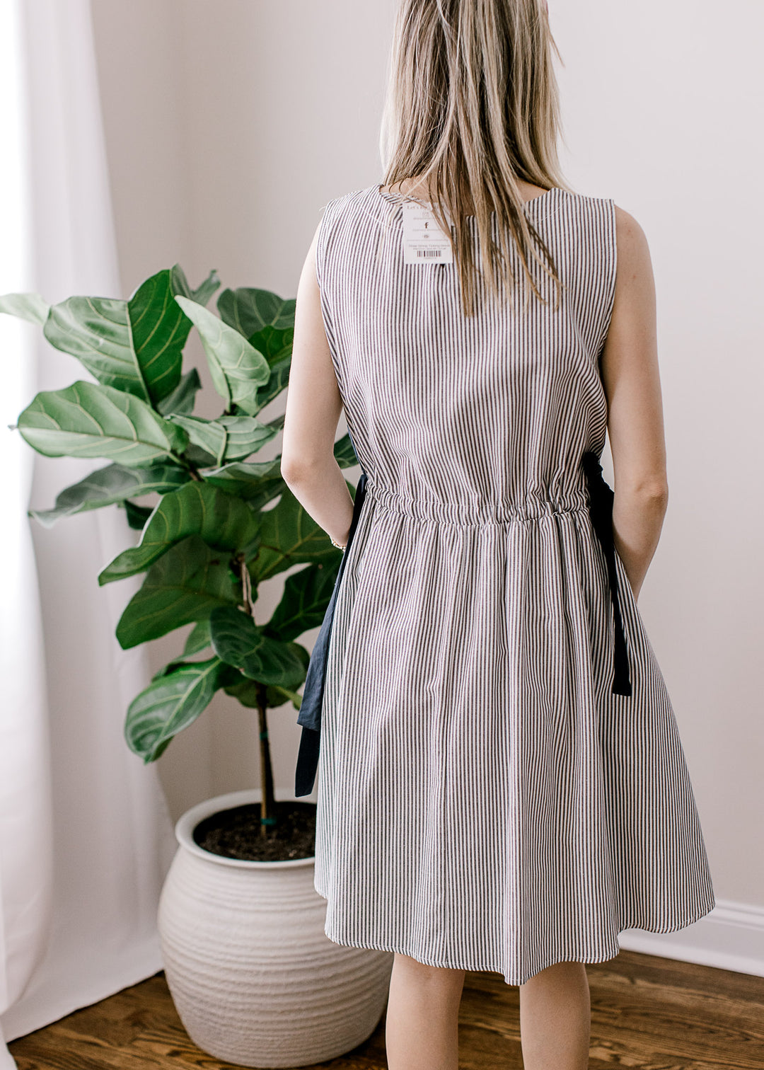 Back view of Model wearing a sleeveless black and white striped dress with a boat neck and pockets. 