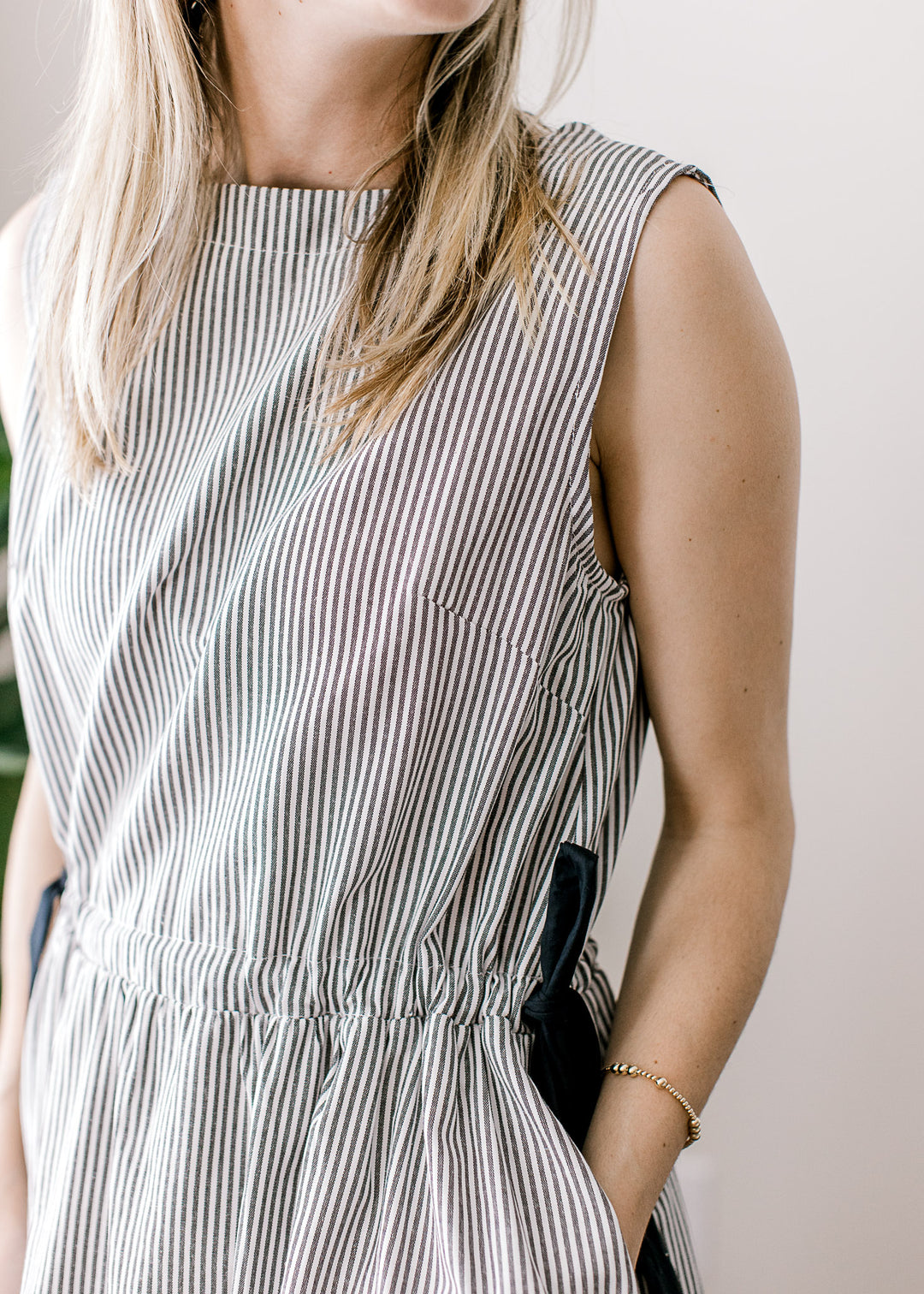 Close up of side ties and pockets on a black and white sleeveless striped dress. 
