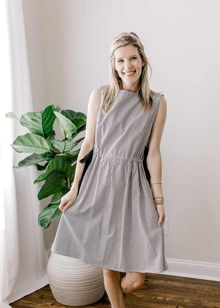 Model wearing a black and white striped above the knee dress with a boatneck and pockets. 
