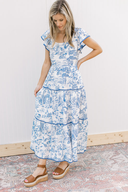 Model wearing a maxi with a toille pattern, tiered design, square neck and flutter short sleeves.