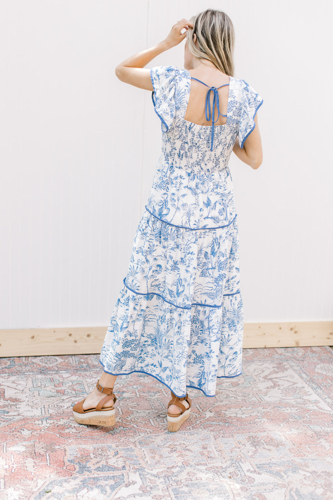 Back view of model wearing a maxi with a toille pattern, tiered design, and tie in back.