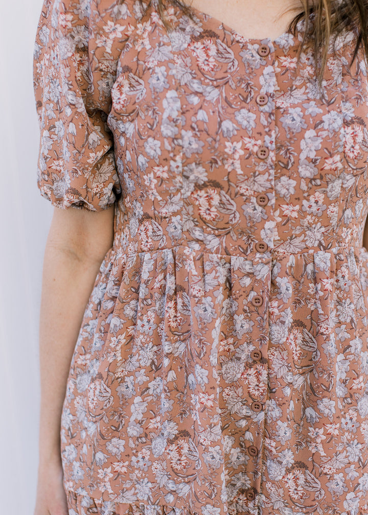 Close up of button front and short sleeves on a burgundy polyester dress with a floral pattern. 