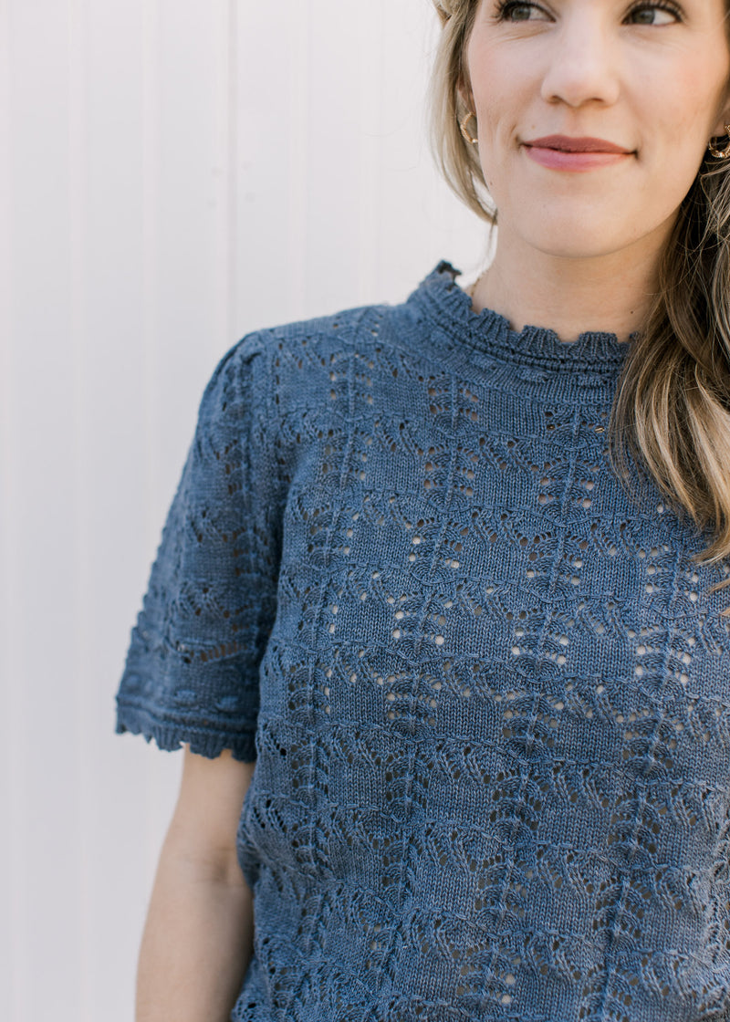 Close up of ruffle detail at the neck and cuff of a dusty blue open weave sweater.