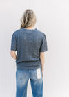 Back view of Model wearing a dusty blue open weave top with ruffles at the neck, cuff and hem.
