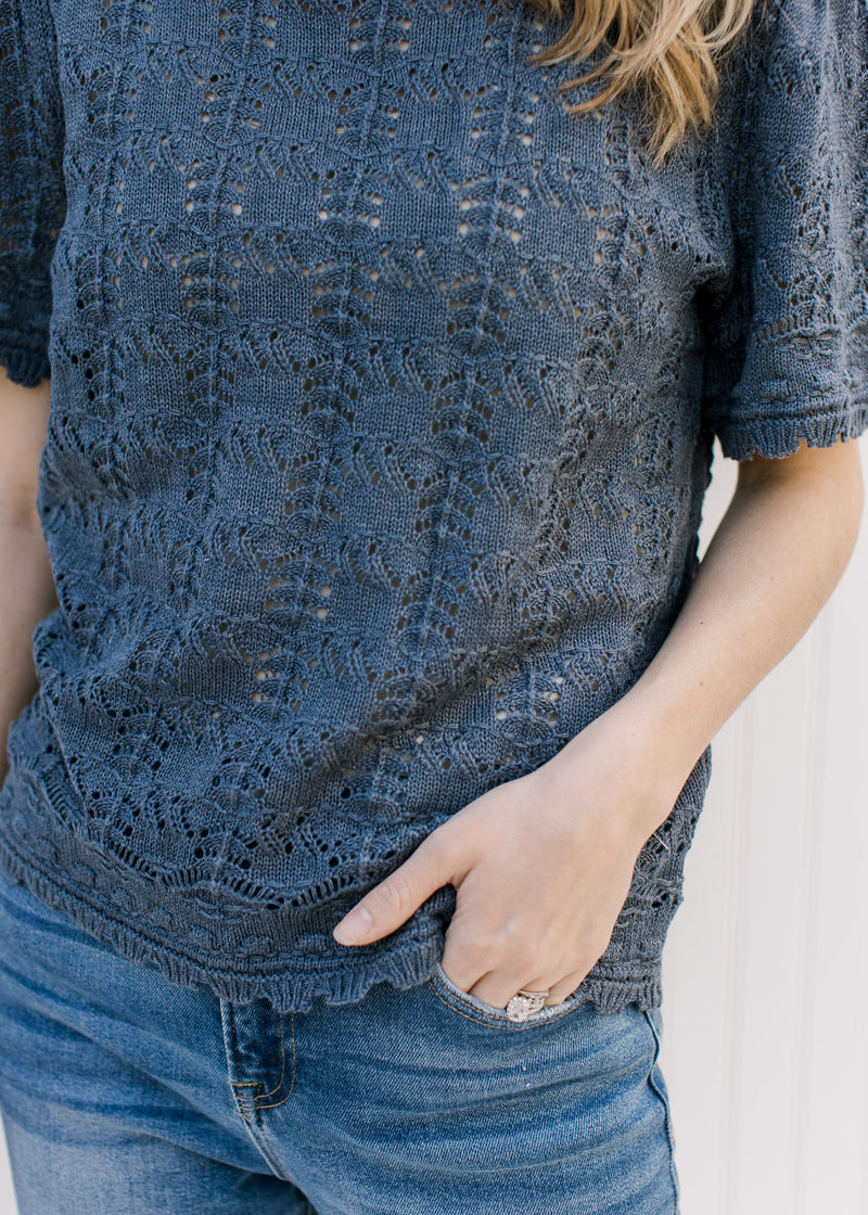 Close up of open weave and ruffle at the hem and cuff of a dusty blue short sleeve sweater.