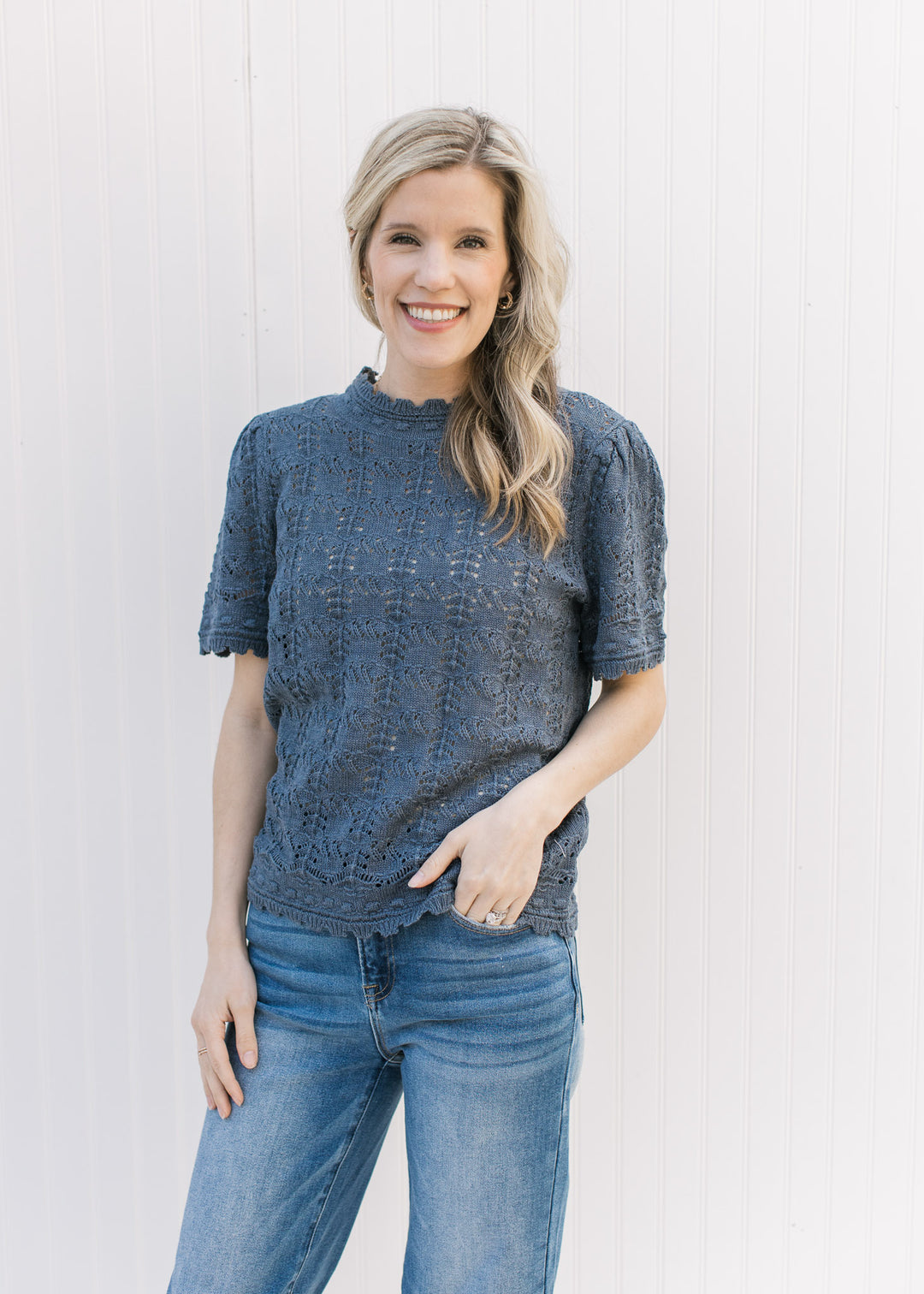 Model wearing a dusty blue open weave top with ruffles at the neck, cuff and hem.