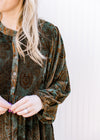 Close up on button front and 3/4 batwing sleeves on a green above the knee dress with brown floral.