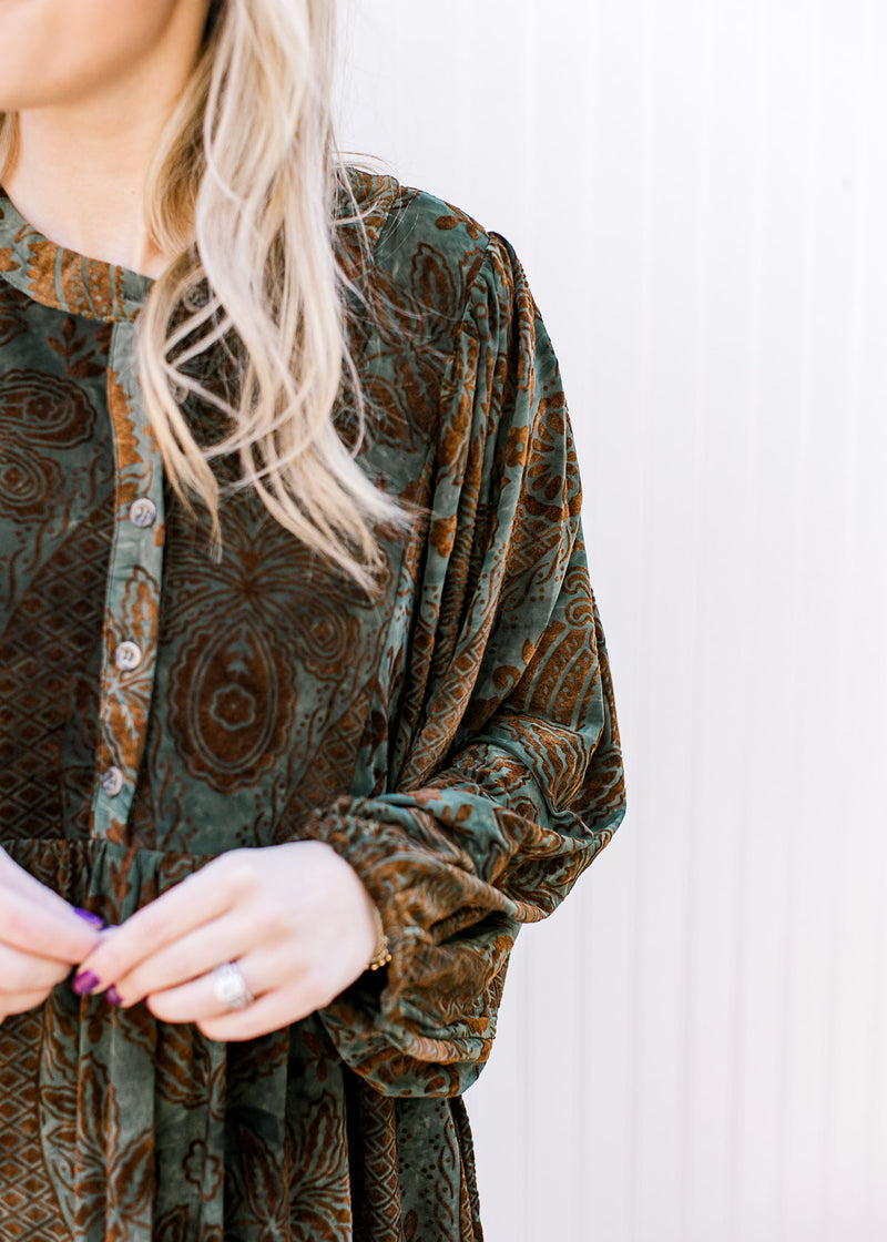 Close up on button front and 3/4 batwing sleeves on a green above the knee dress with brown floral.