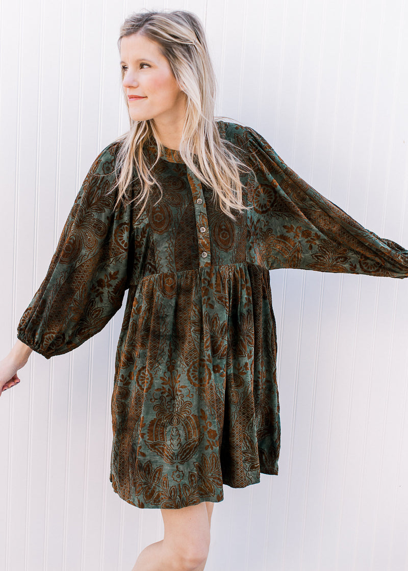 Model wearing a green dress with brown floral, 3/4 batwing sleeves and velvet material.