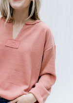Close up of v-neck and patchwork detail on an apricot colored top with cuffed sleeves.