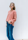 Model wearing jeans with a v-neck apricot top with a cuffed sleeve and patchwork detail.