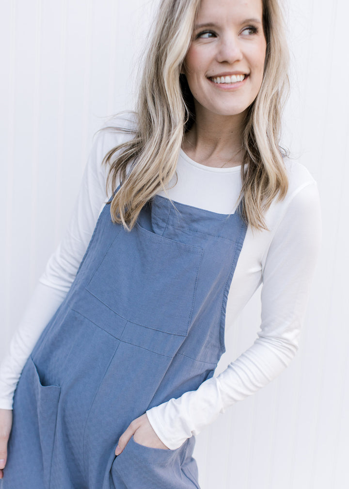 Model wearing a dusty blue jumpsuit with adjustable straps and front patch pocket. 