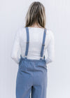 Back view of model in a dusty blue jumpsuit with adjustable straps and an elastic waistband.