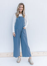 Model wearing a dusty blue jumpsuit with a white top and mules. 