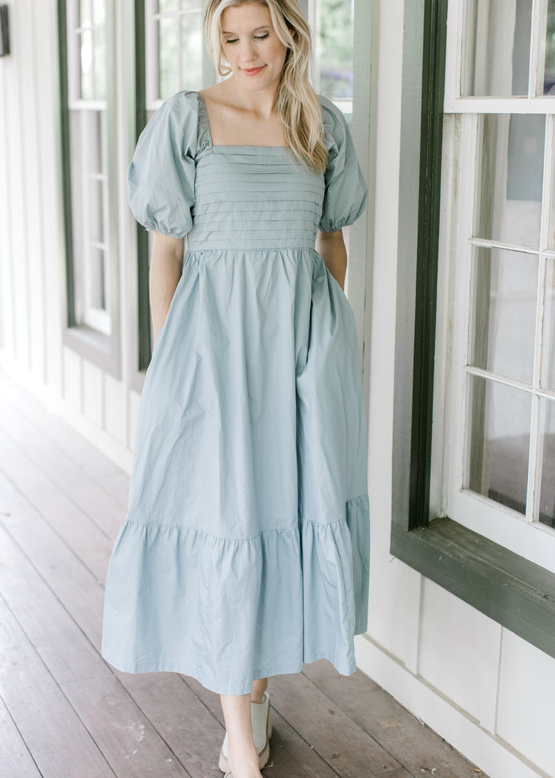 Model wearing a pale blue midi with a pleated bust, smocked back and short bubble sleeves. 