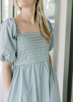 Close up of square neckline, pleated bust and short bubble sleeves on a pale blue midi with pockets.