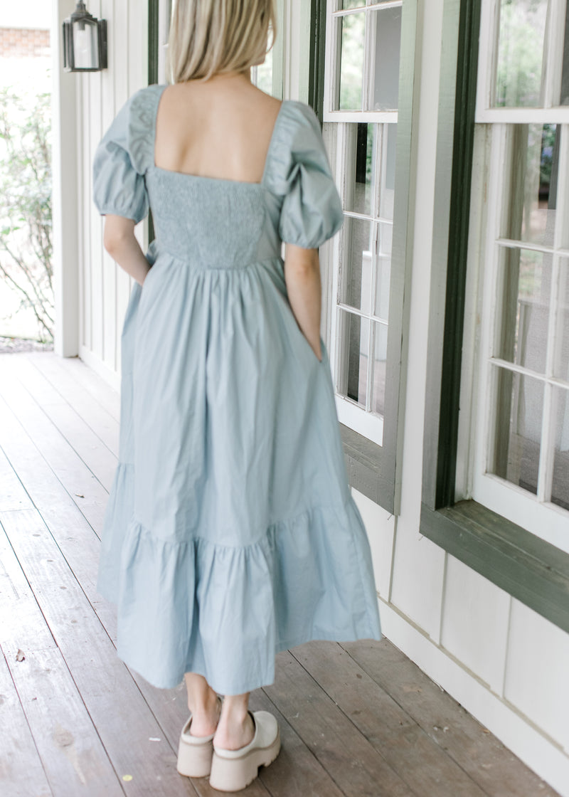 Back view of Model wearing a pale blue midi with a smocked back and short bubble sleeves. 