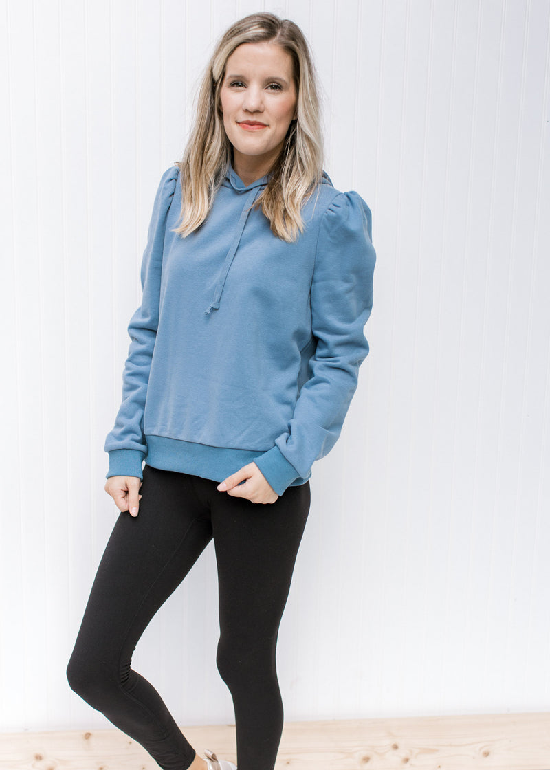 Model wearing leggings with a dusty blue pullover with puff shoulders, long sleeves and a hoodie. 
