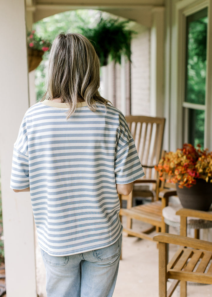 Back view of Model wearing a short sleeve dusty blue and white striped top with pale yellow neck.