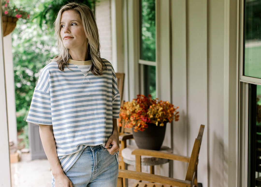 Model wearing jeans and a short sleeve dusty blue and white striped top with pale yellow round neck.
