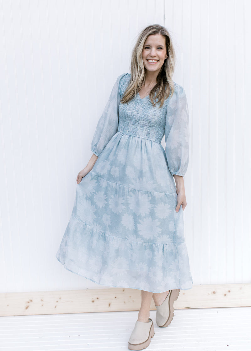 Model wearing a sage dress with a smocked bodice, 3/4 sheer sleeves and a faint daisy print.