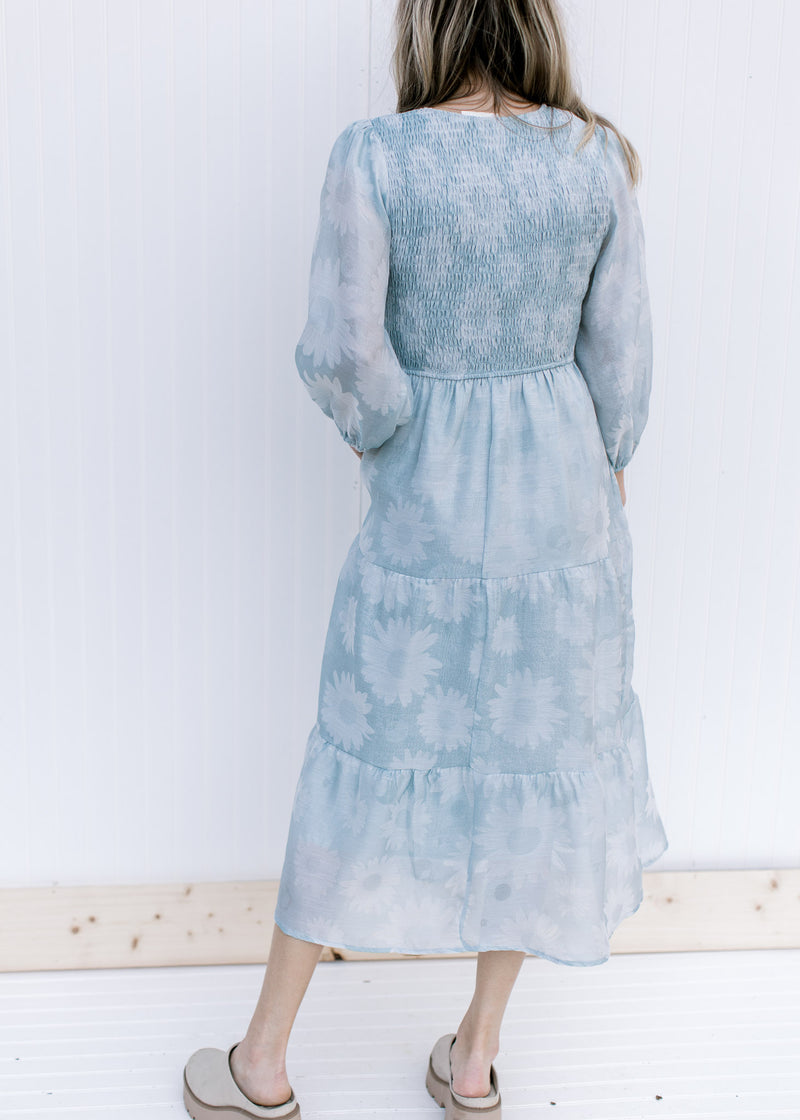 Back view of Model wearing a sage dress with a smocked bodice, 3/4 sheer sleeves and a daisy print.