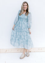 Model wearing a sage dress with a smocked bodice, 3/4 sleeves and a faint daisy print.