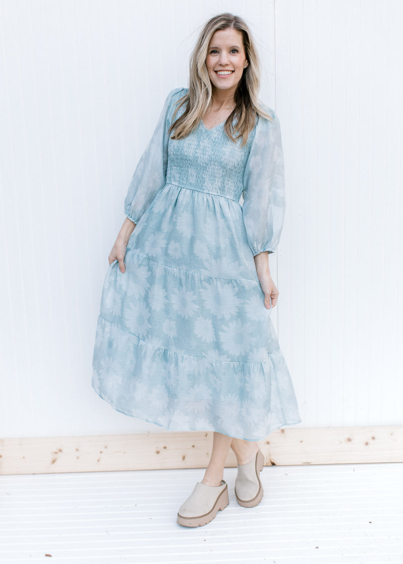 Model wearing a sage dress with a smocked bodice, 3/4 sleeves and a faint daisy print.